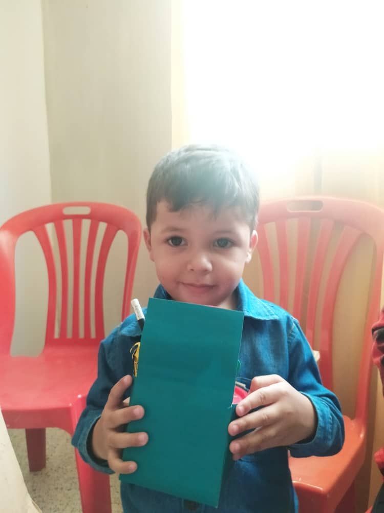 A young boy in a blue shirt is holding a piece of paper