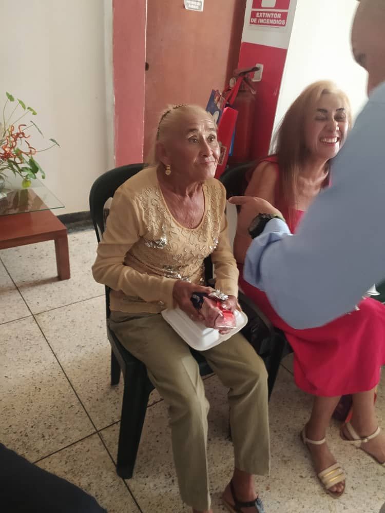 An elderly woman is sitting in a chair talking to a man.
