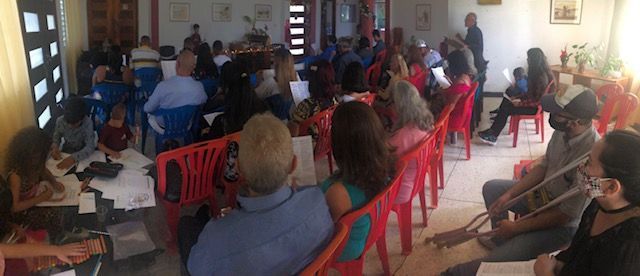 A large group of people are sitting in red chairs in a room.