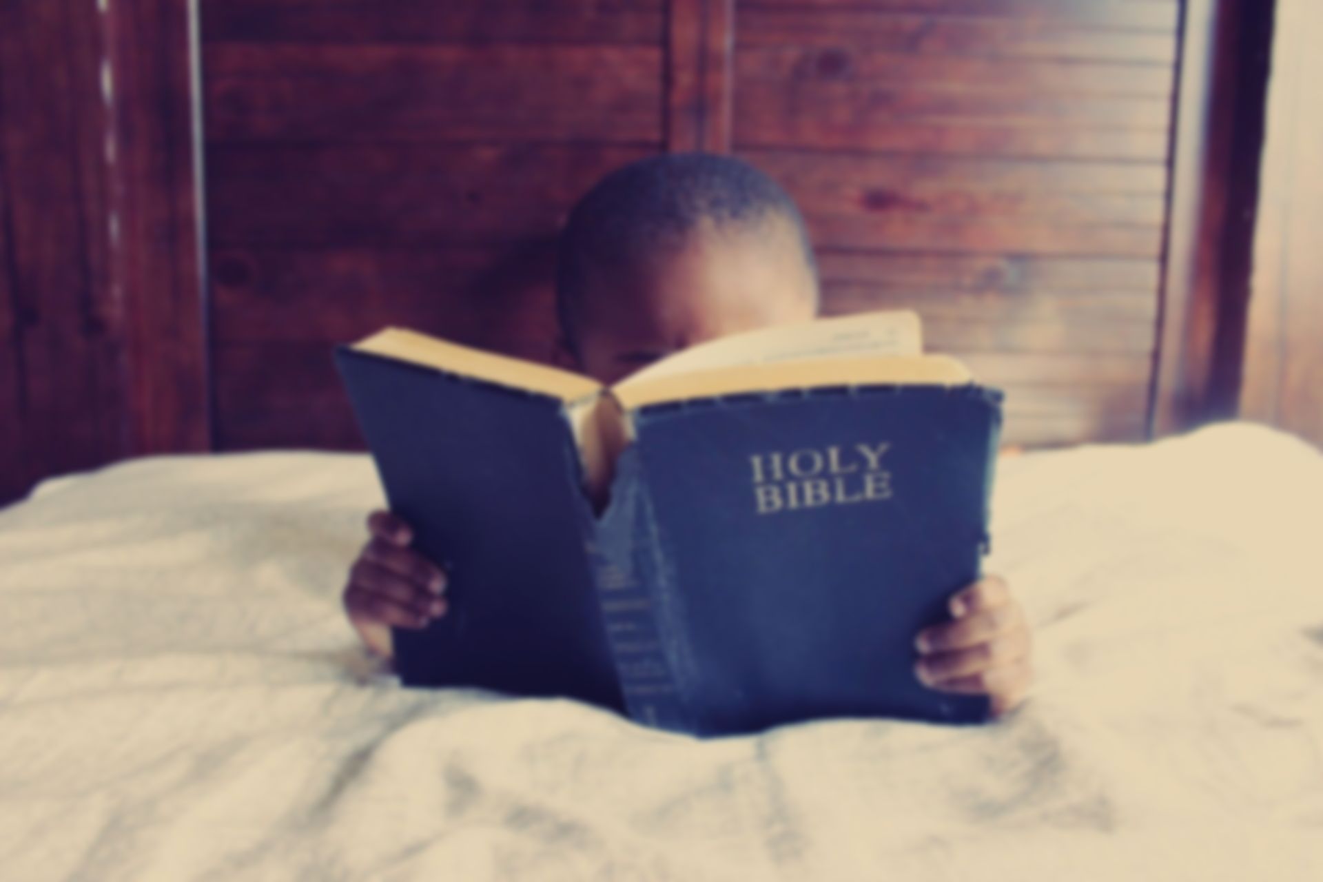 A child is reading a holy bible on a bed