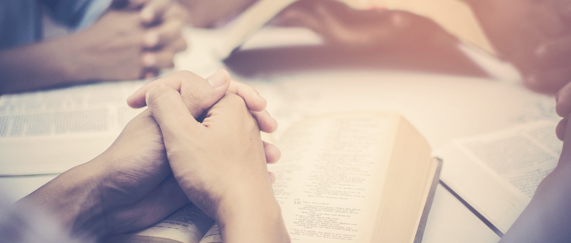 A group of people are holding hands over a bible.