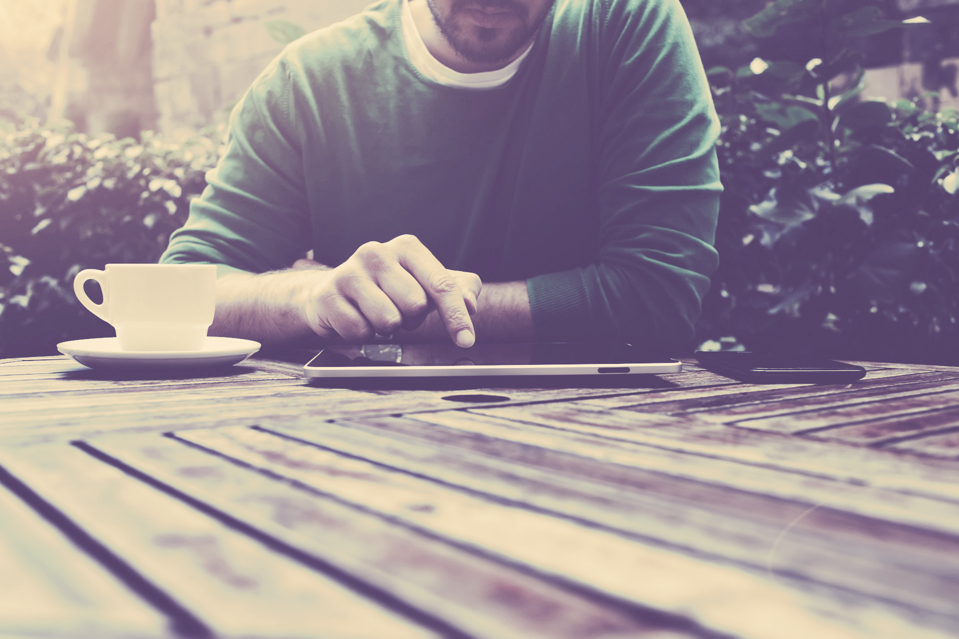 A man is sitting at a table with a cup of coffee and a tablet.