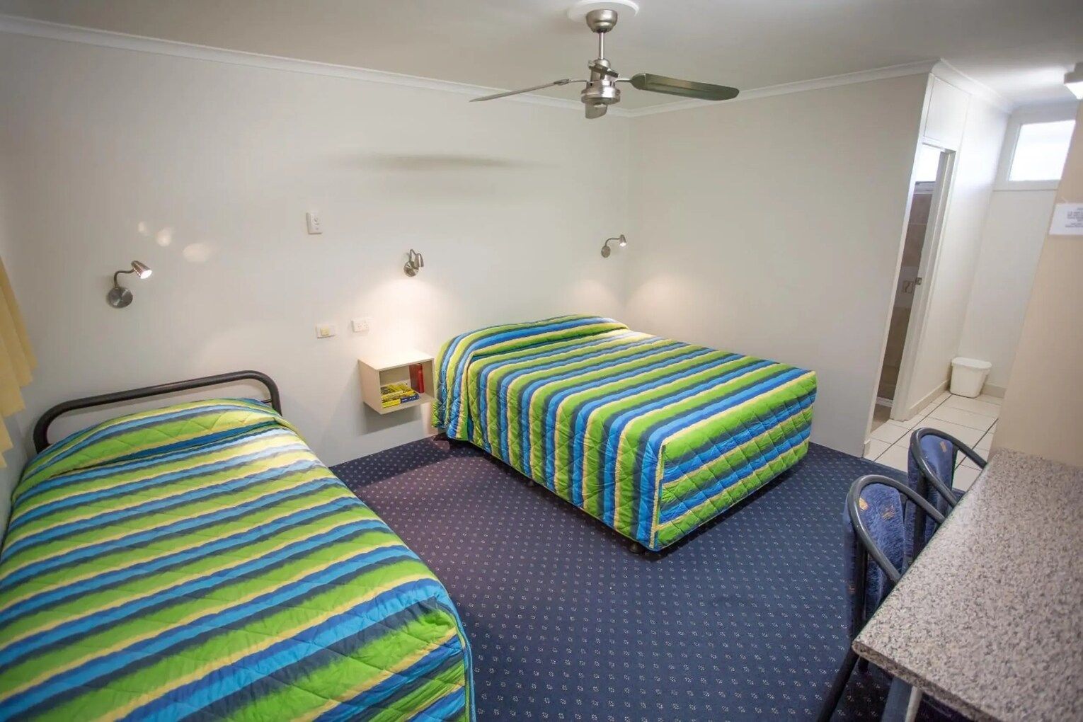 Small Hotel Room: Bed, Blue Recliner, Table, Fridge, Microwave, Tv, Beach Art — Fourth Avenue Motor Inn in Parkside, QLD
