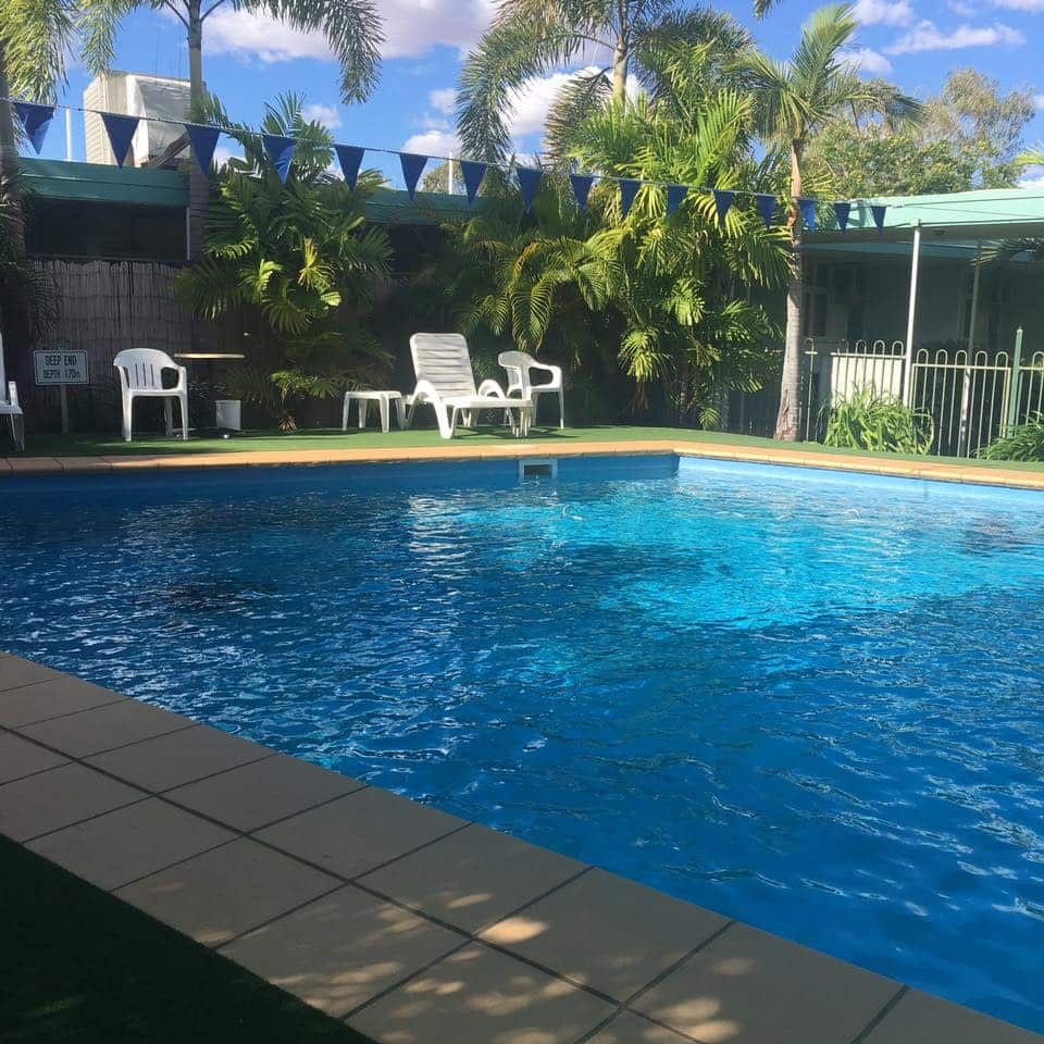 Pool with Blue Water Surrounded by Lounge Chairs and Green Foliage — Fourth Avenue Motor Inn in Parkside, QLD