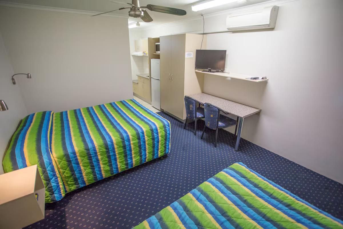 A Motel Room With Two Beds, a Desk, and a Television — Fourth Avenue Motor Inn in Parkside, QLD