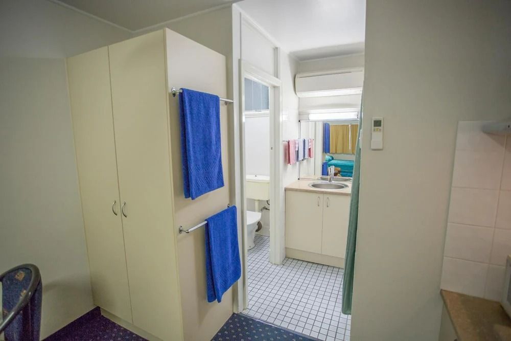 Narrow Room With a Wardrobe, Blue Towels, and a View Into a Small Bathroom — Fourth Avenue Motor Inn in Parkside, QLD