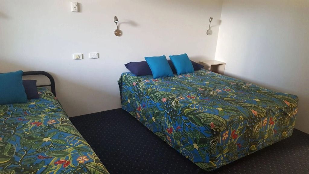 Two Beds in a Motel Room With Floral Bedspreads, Blue Pillows, and Off-white Walls — Fourth Avenue Motor Inn in Parkside, QLD