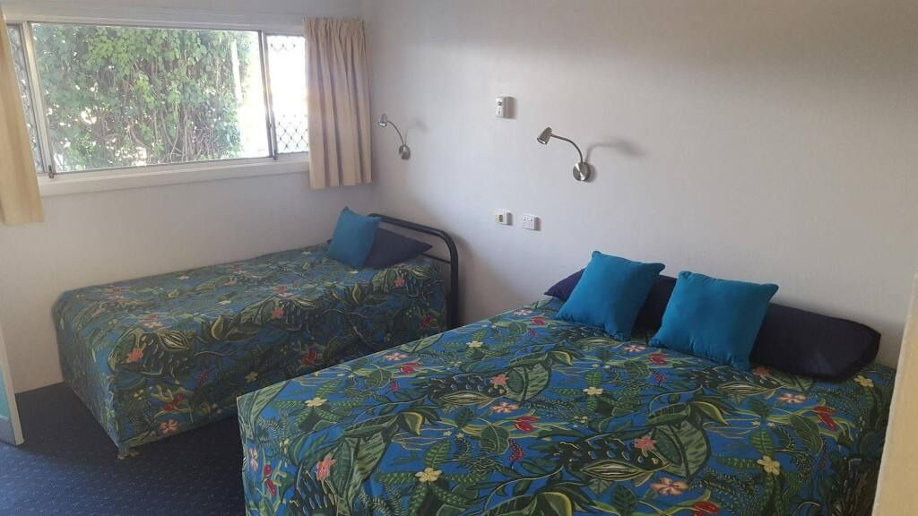 A Motel Room With Two Beds Covered in a Blue Floral Pattern, a Window and Lamps — Fourth Avenue Motor Inn in Parkside, QLD