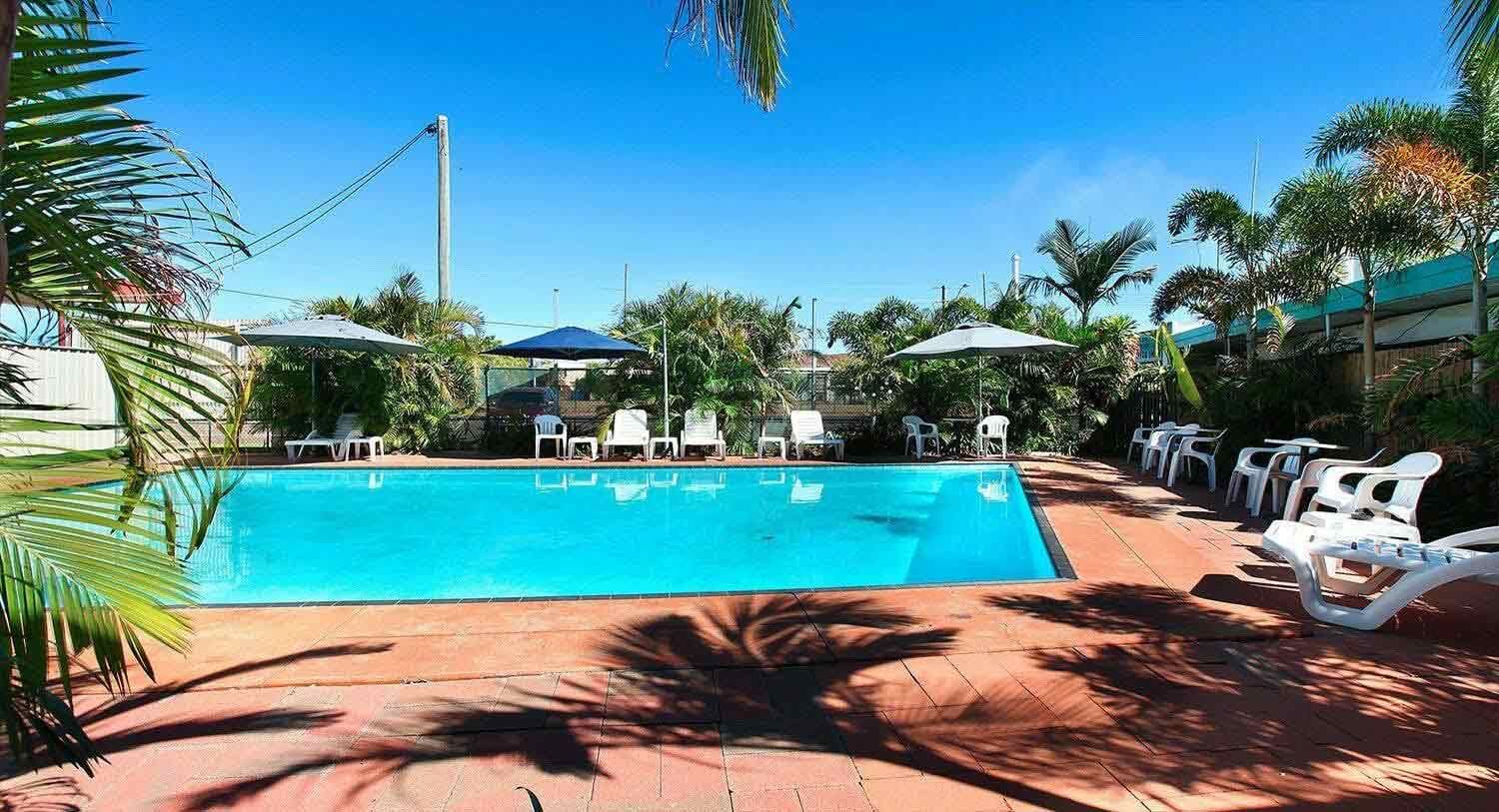 Swimming Pool With Lounge Chairs and Umbrellas Under a Clear, Blue Sky — Fourth Avenue Motor Inn in Parkside, QLD