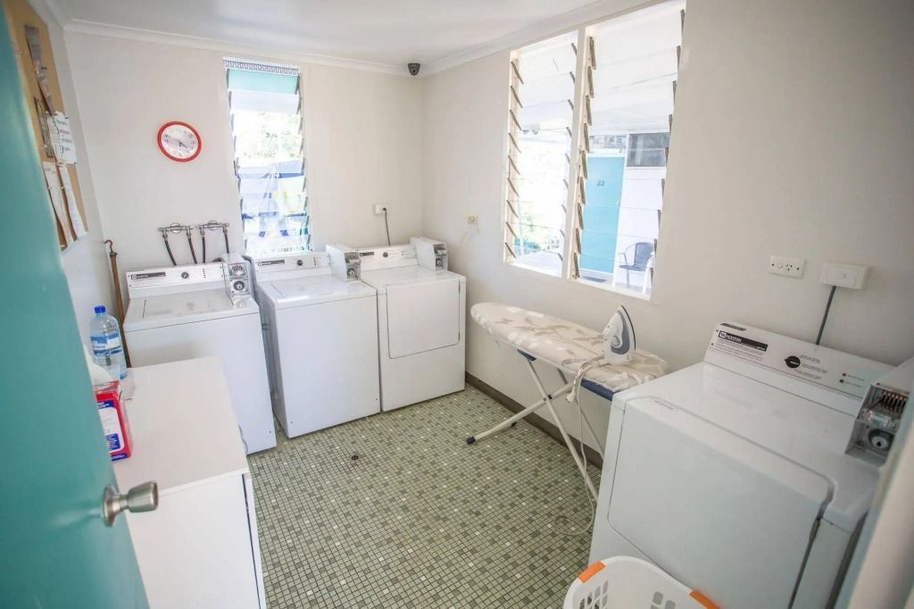 Laundry Room With Washers, Dryer, Ironing Board, and a Round Clock — Fourth Avenue Motor Inn in Parkside, QLD