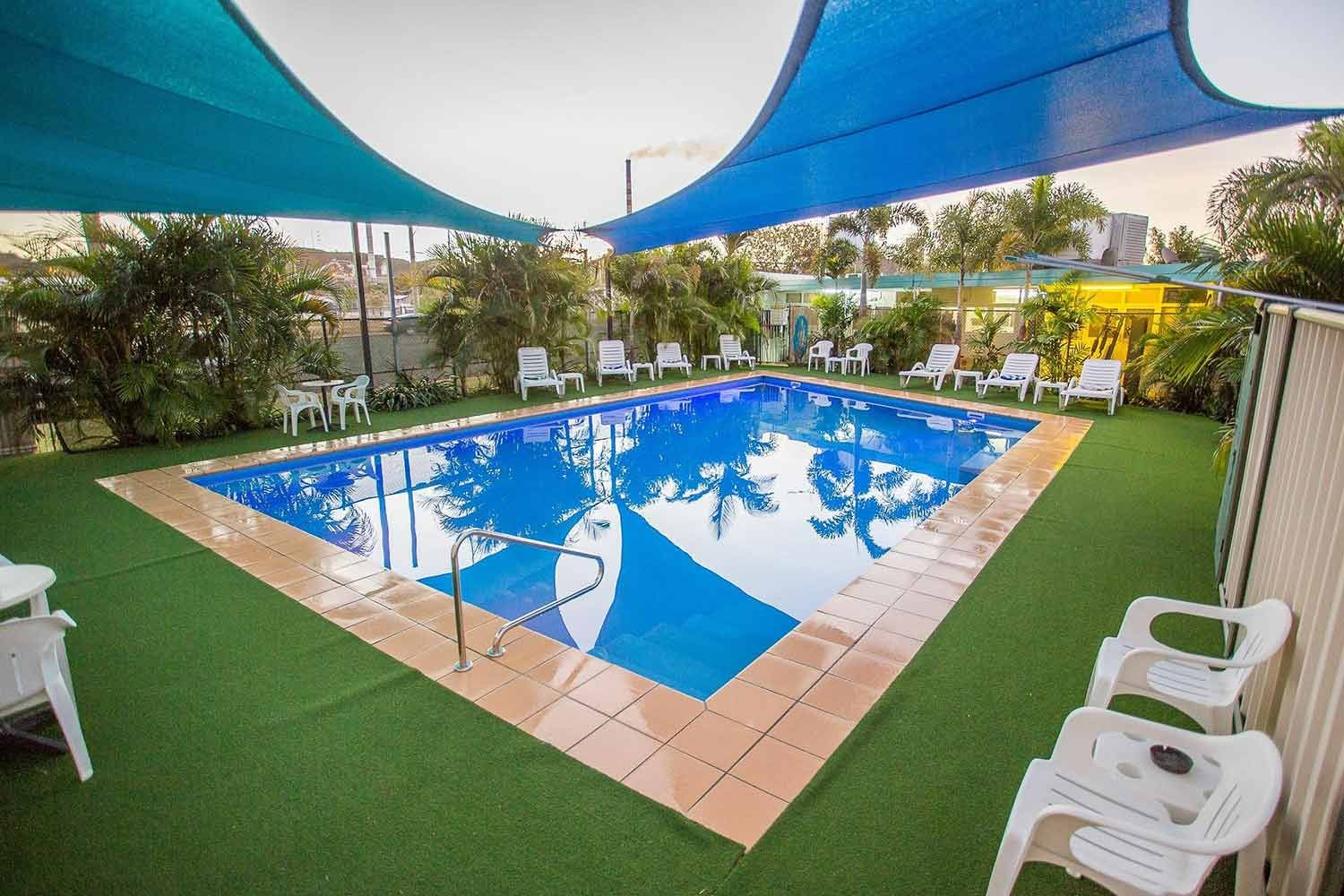Rectangular Pool With Blue Shades, White Chairs, and Artificial Green Grass — Fourth Avenue Motor Inn in Parkside, QLD
