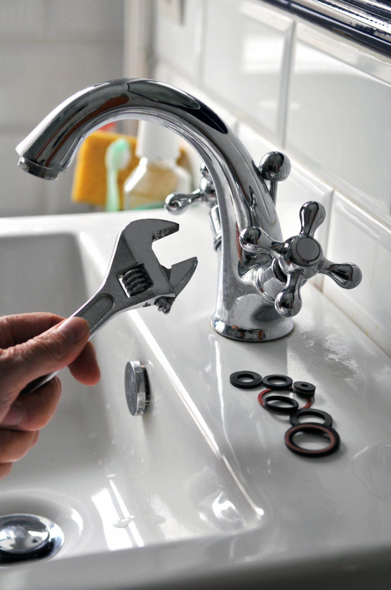 Person using a wrench to repair a chrome faucet in a white bathroom sink.
