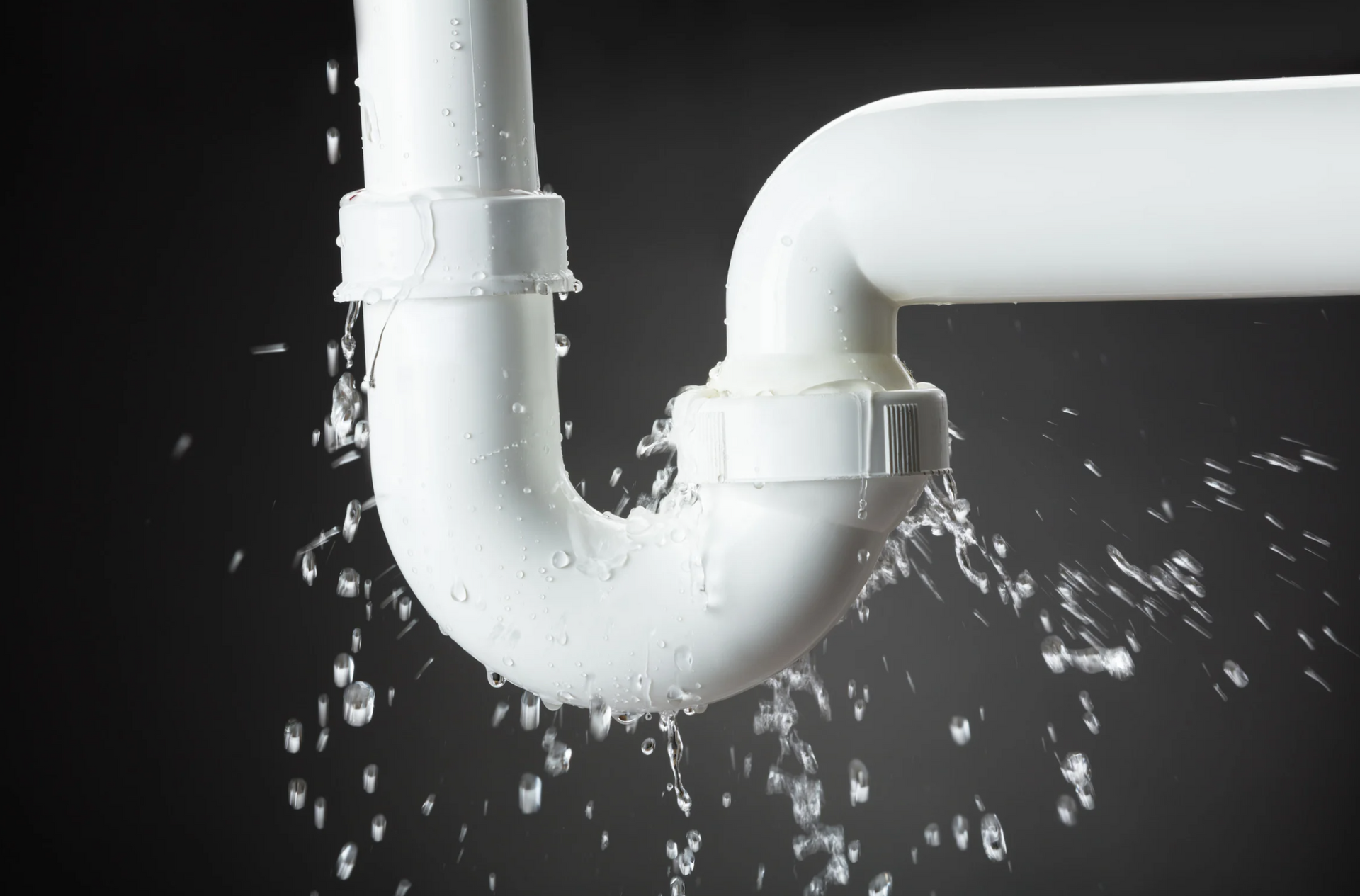 Leaking white PVC pipe with water spraying out against a black background.