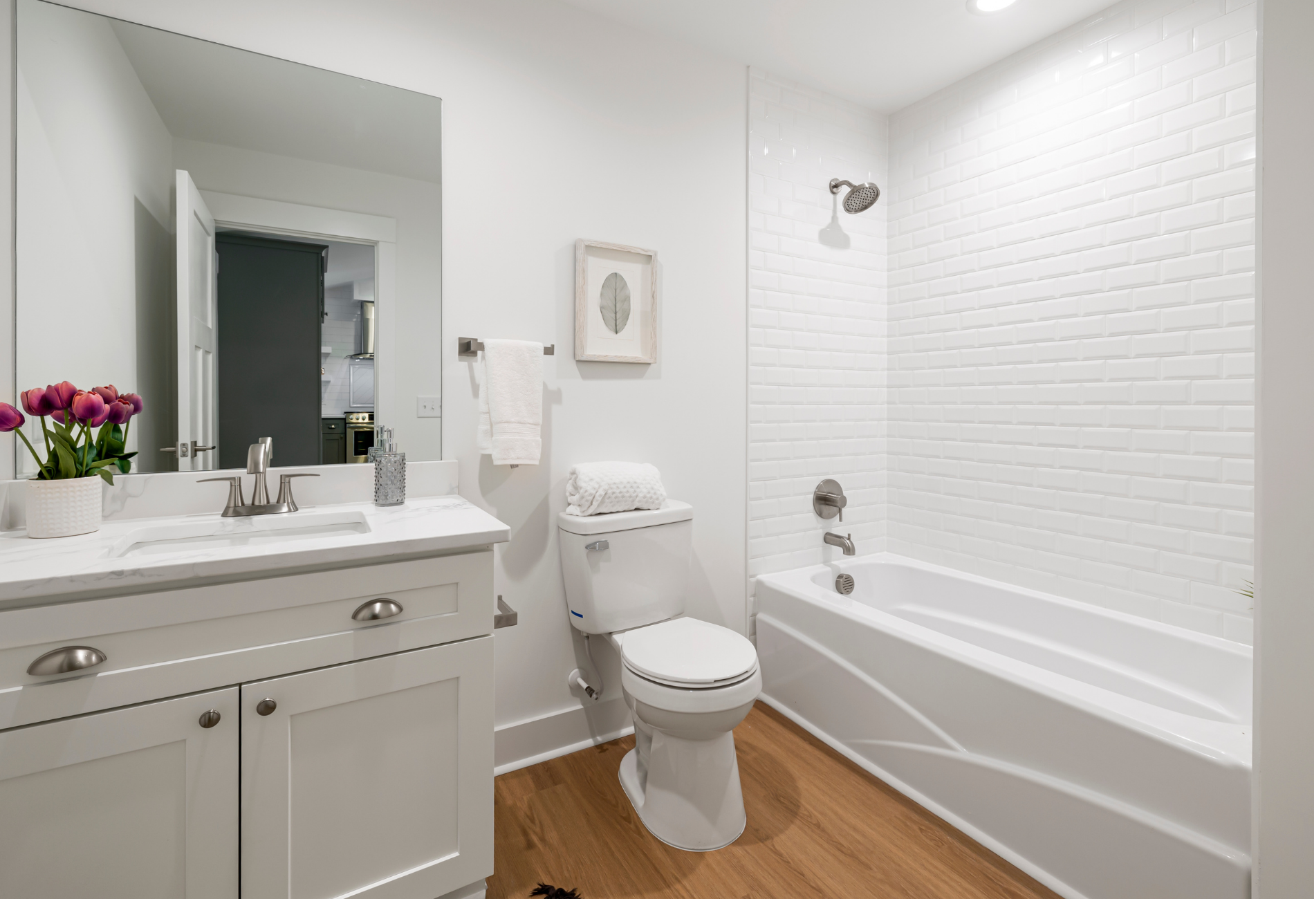 White bathroom with sink, toilet, tub, and wooden floor.