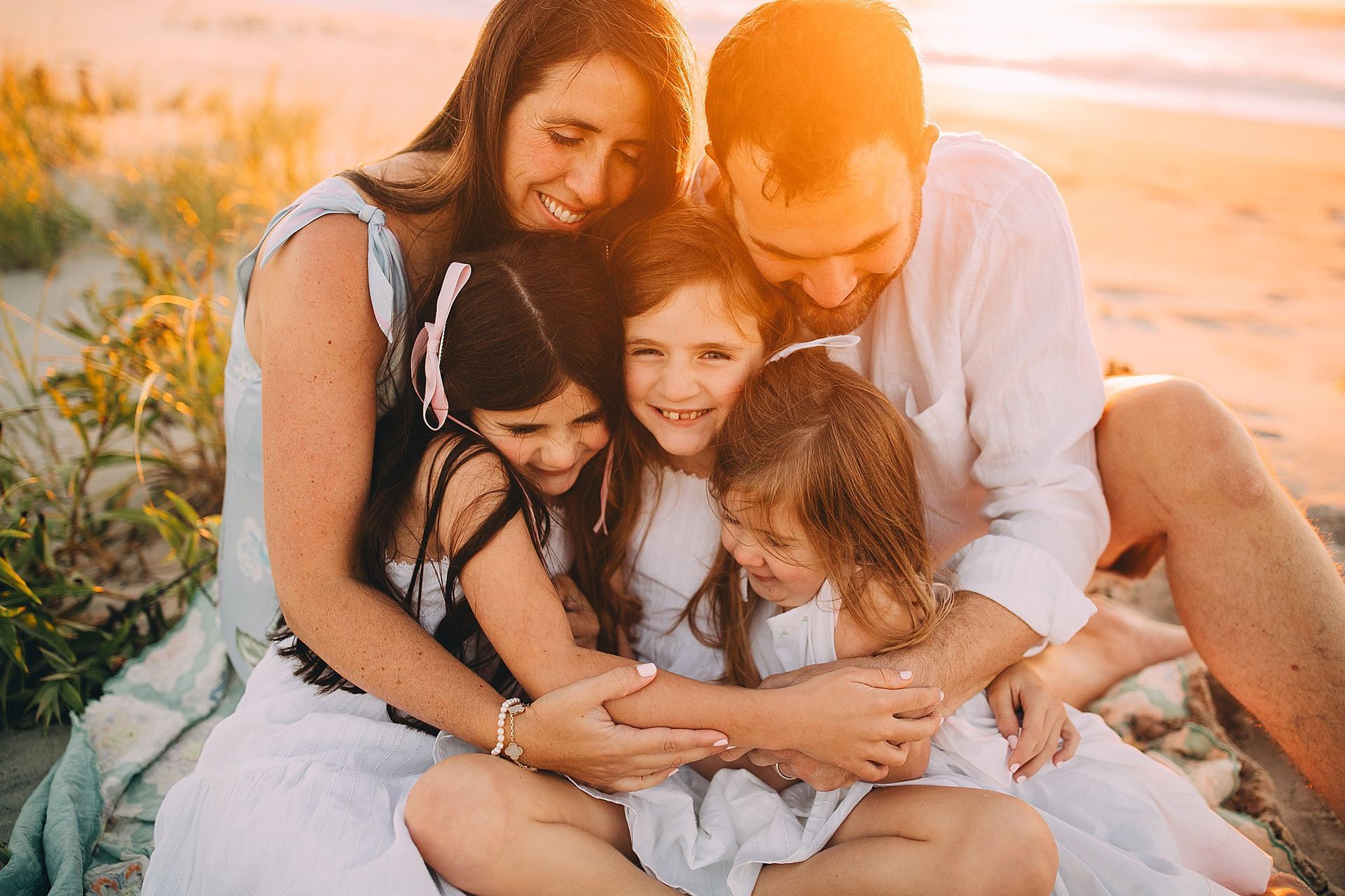 Family of five embracing on a beach, smiling in sunlight.