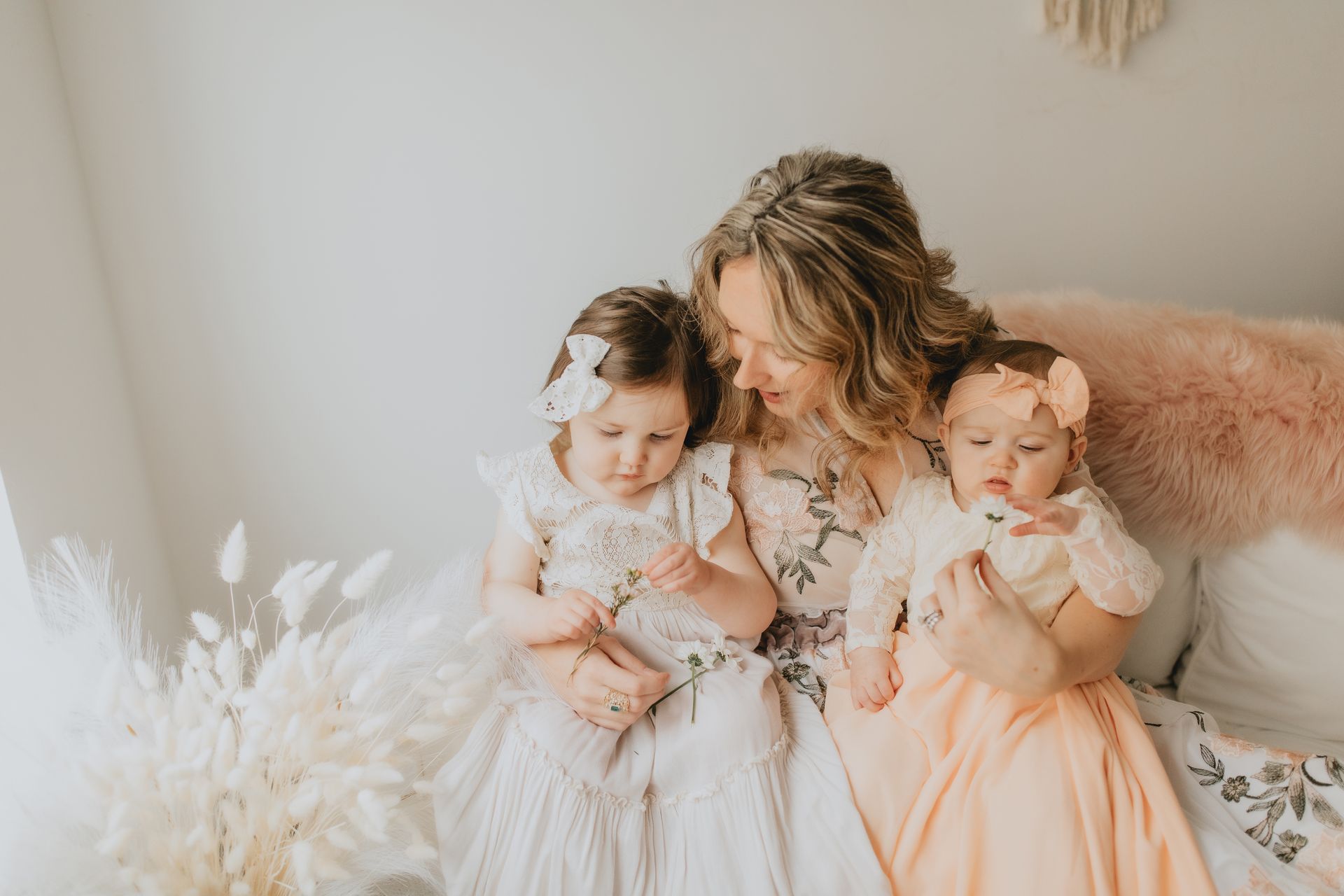 Woman sitting with two babies on a bed, looking down. Natural light.