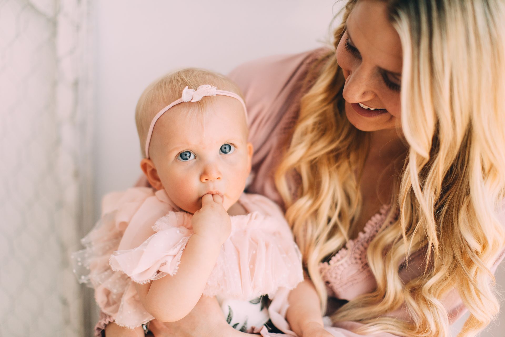 Mother holding baby, both in pink, baby sucking thumb.