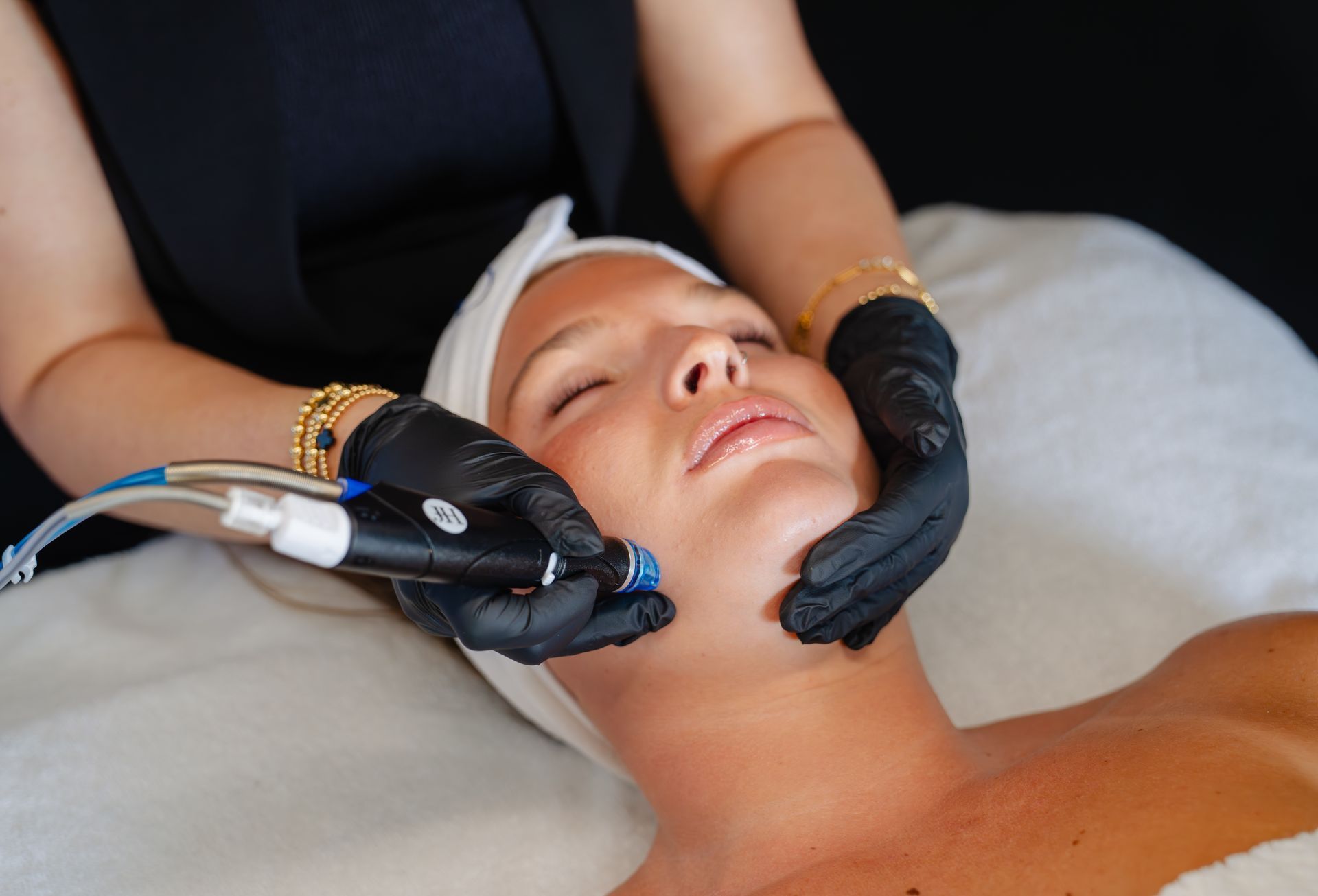 Woman receiving facial treatment with gloved hands and a handheld device.