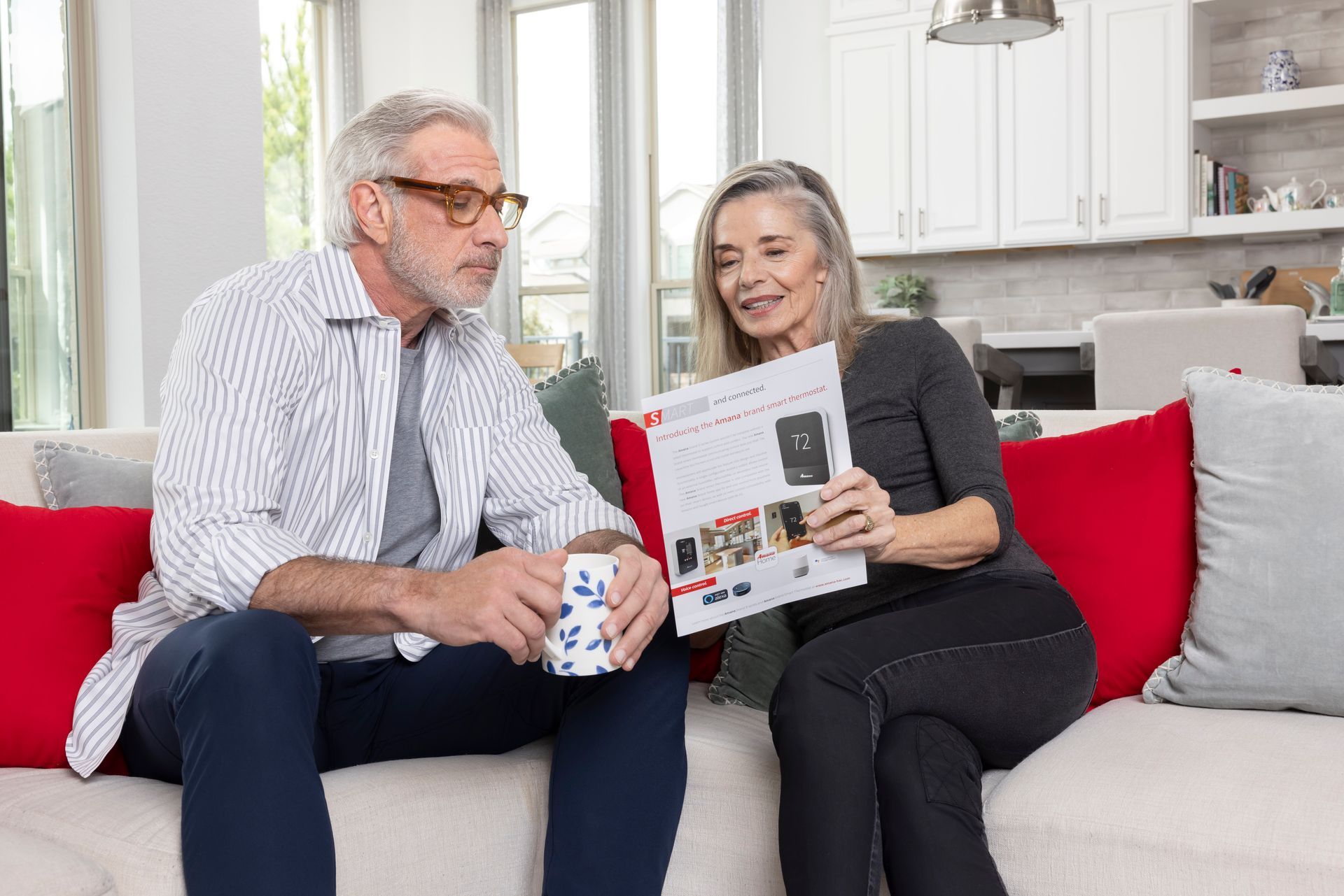 A man and a woman are sitting on a couch reading a magazine.