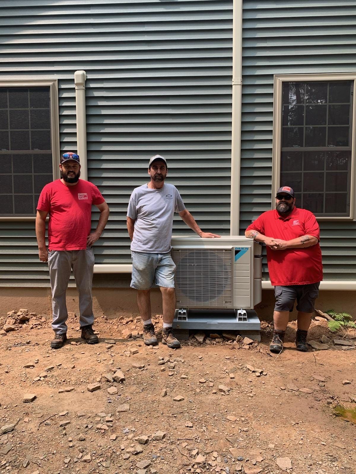 Three men are standing next to each other in front of a house.