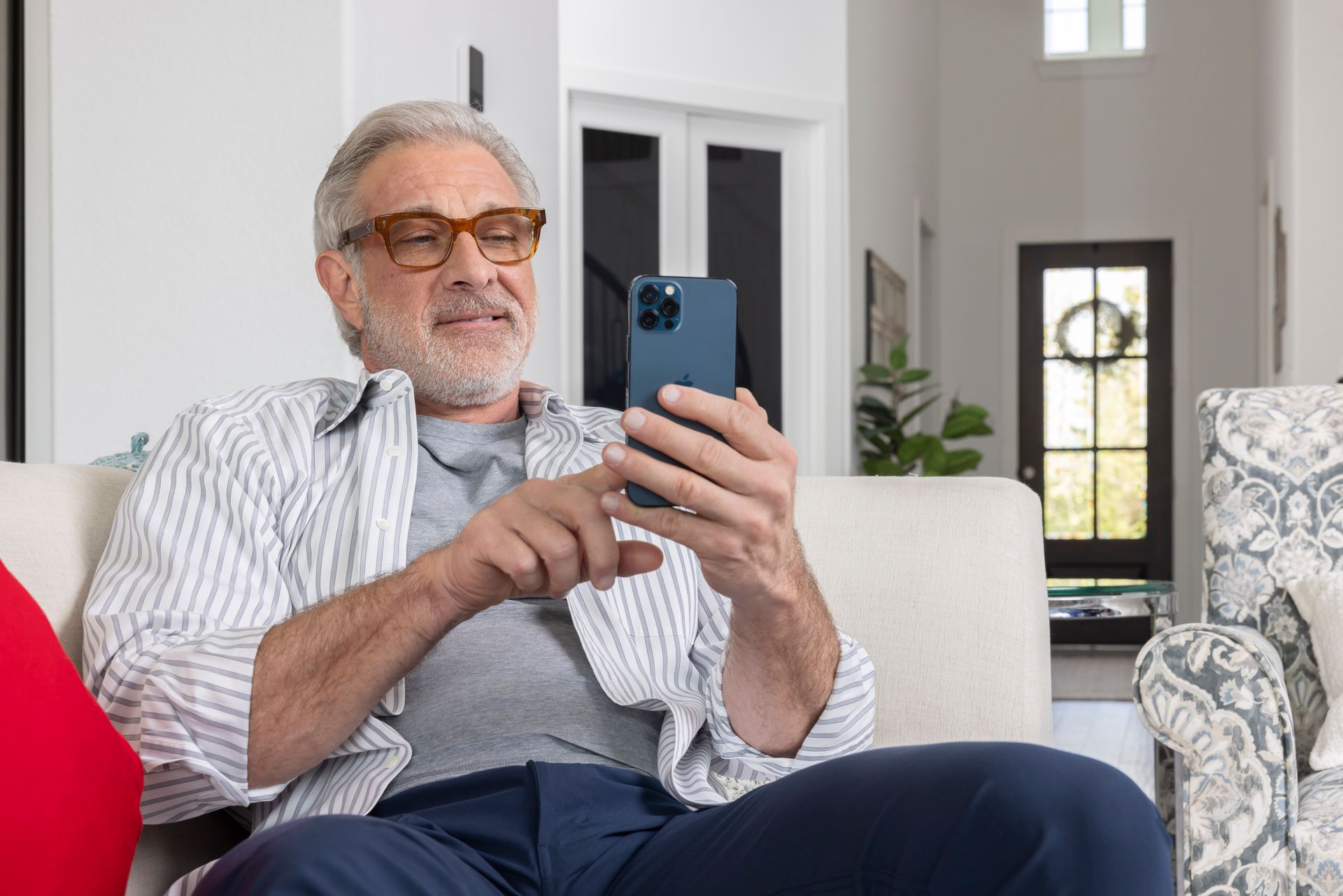 An older man is sitting on a couch looking at his cell phone.