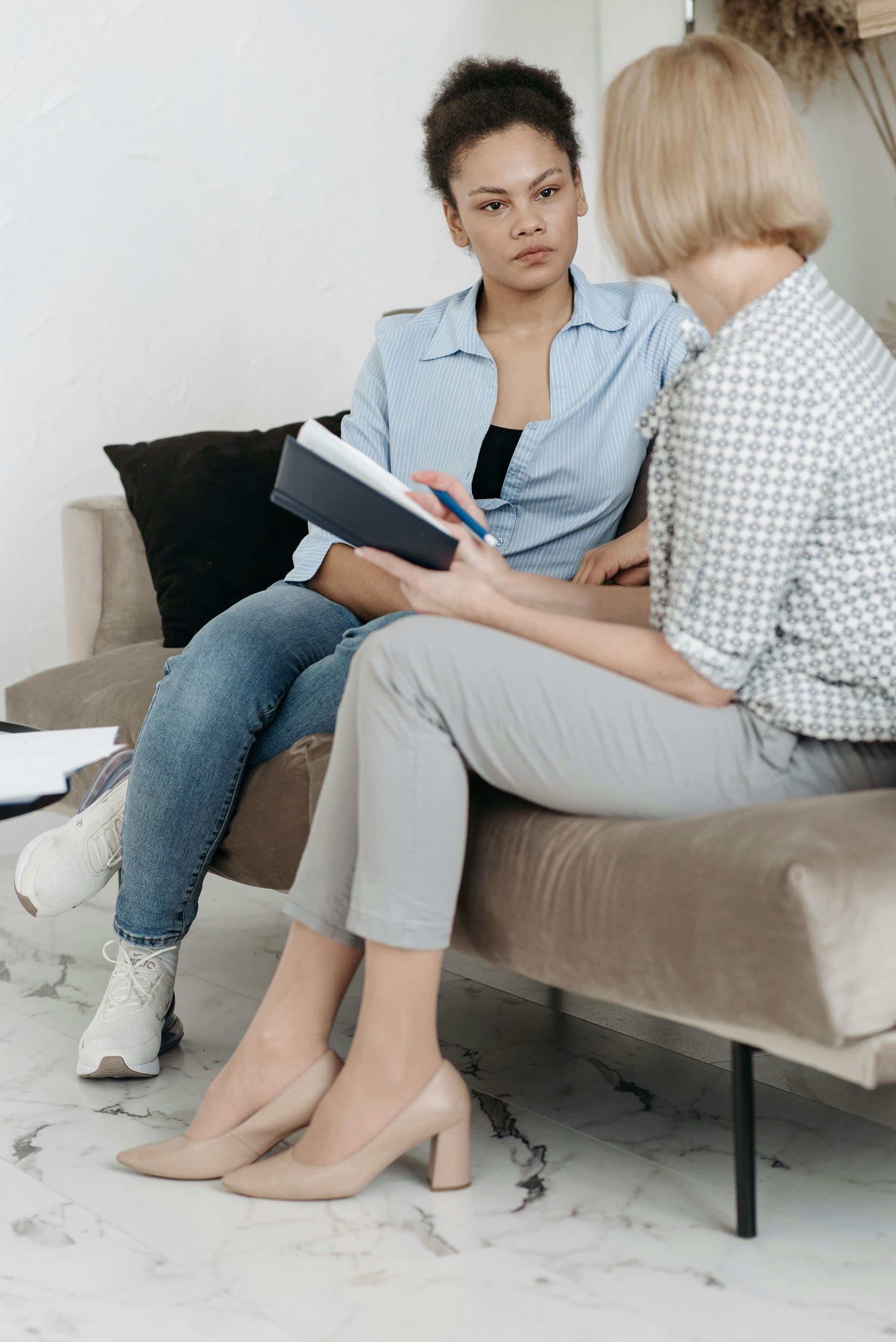 Two women are sitting on a couch talking to each other.