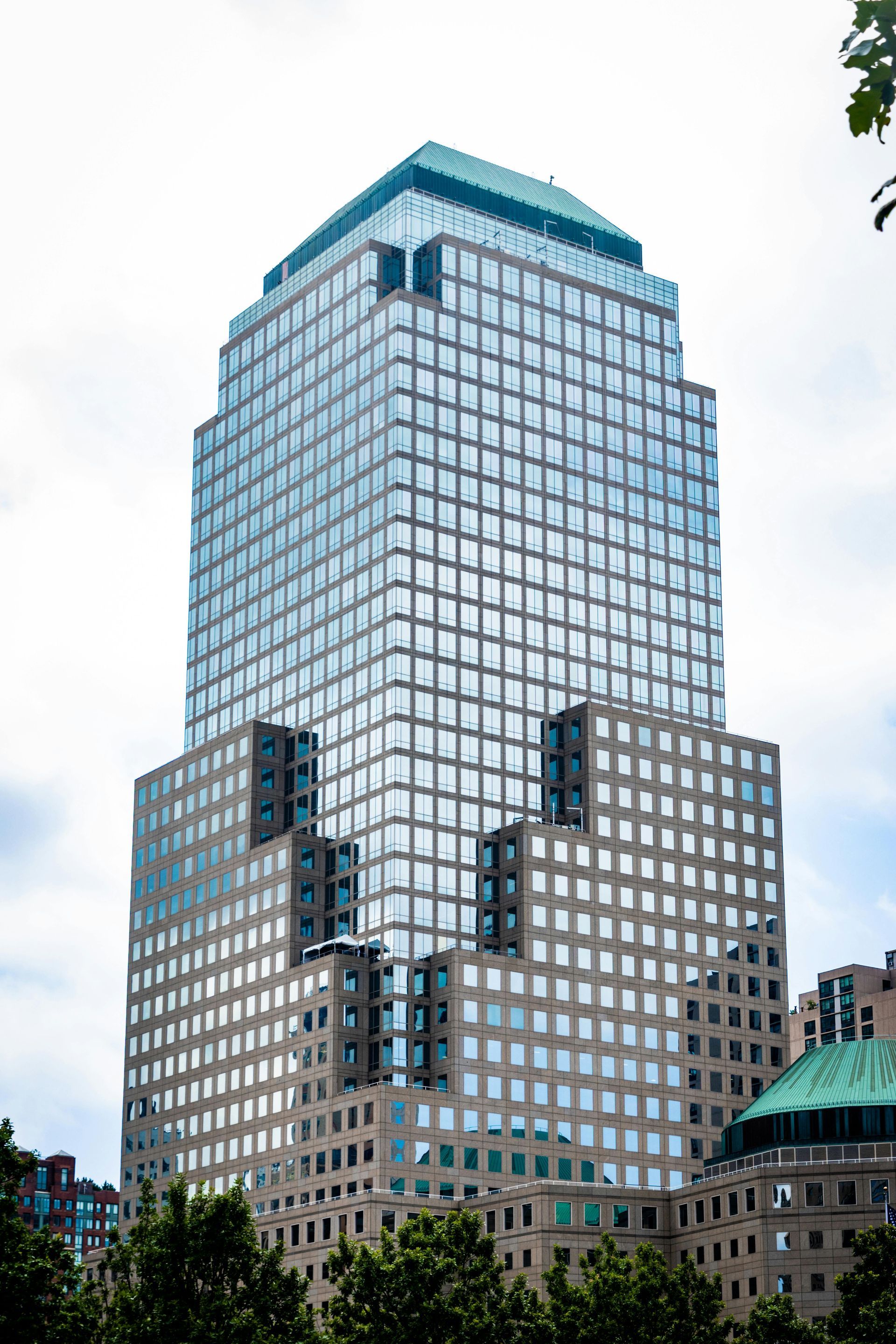 High-rise office building with a blue-green glass top and a facade of reflective windows against a cloudy sky.