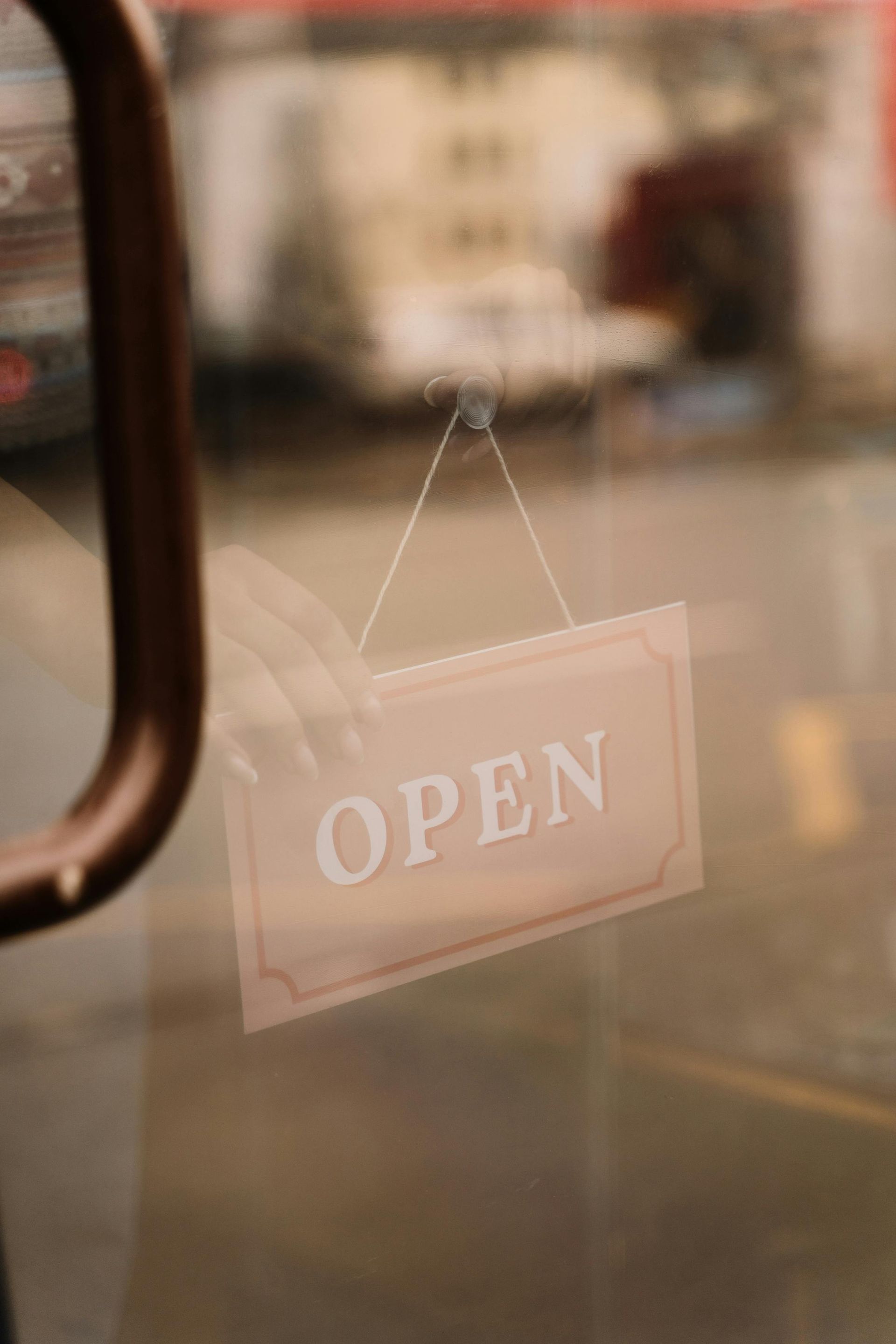 Open sign hanging on a glass door, with a hand adjusting it, blurred background.