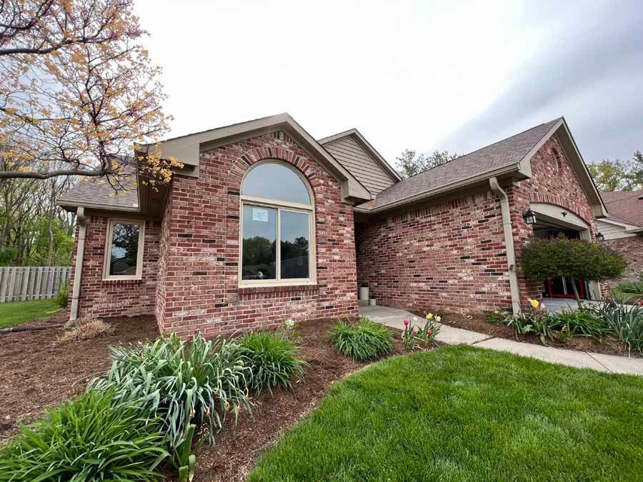 A brick house with arched windows and a lush green lawn in front of it.