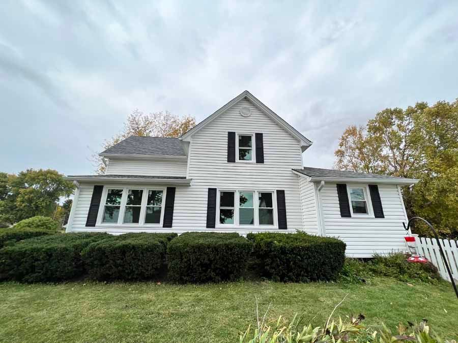 A white house with black shutters and a fence in front of it.