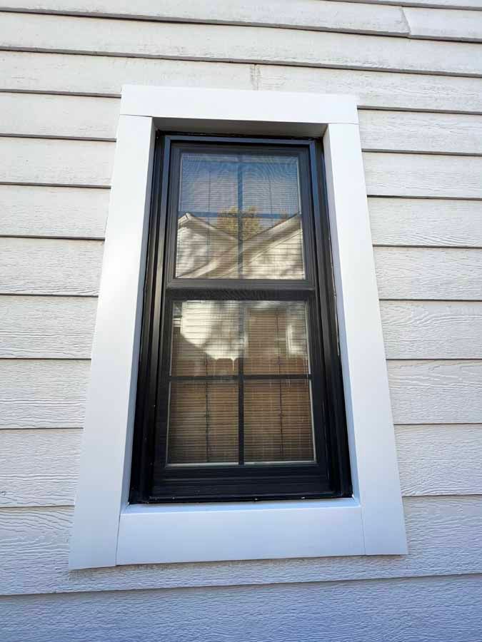 A black window is on the side of a white house.