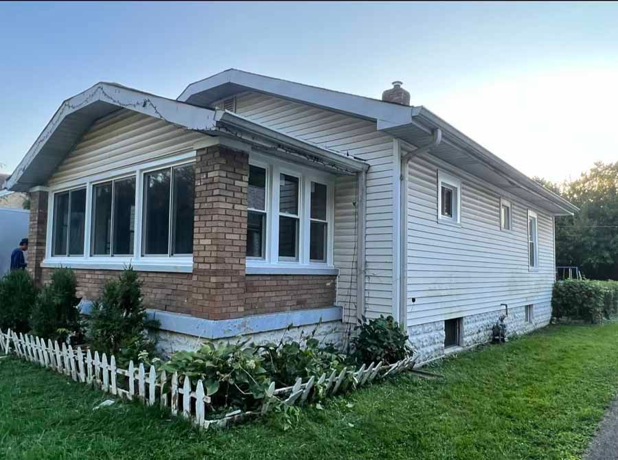 A white house with a brick facade and a white picket fence in front of it.