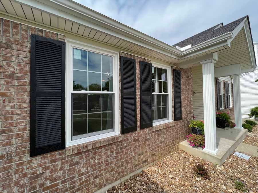 A brick house with black shutters on the windows and a porch.