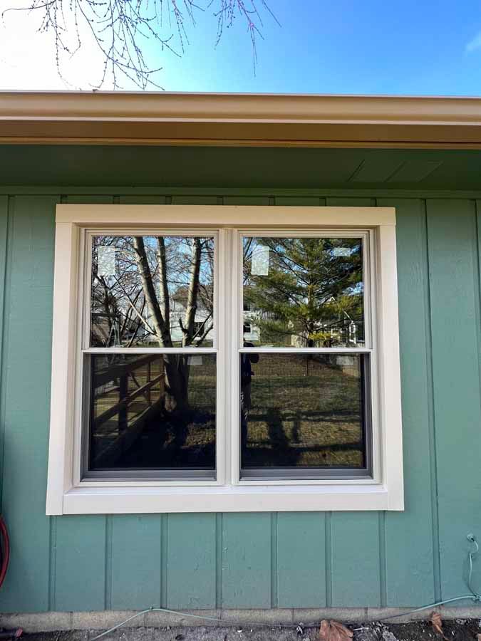 A green house with a white window and a reflection of trees in the window.