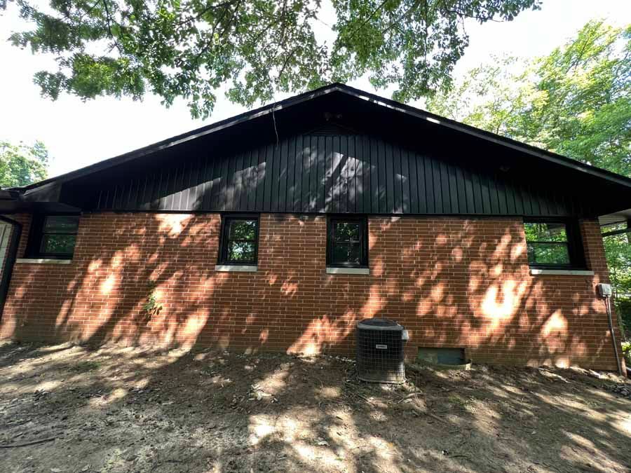 A brick house with a black roof is surrounded by trees.
