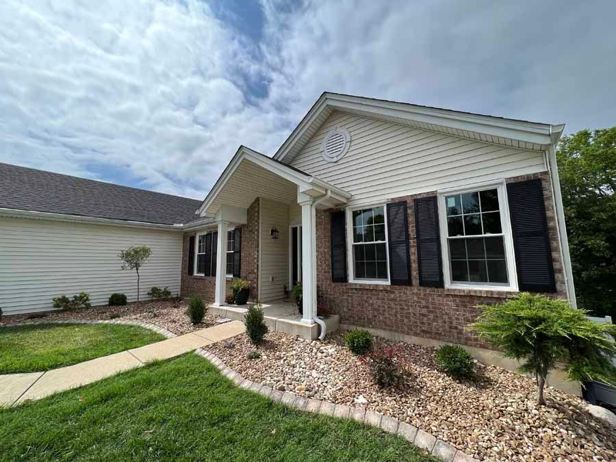 A white house with a brick roof and black shutters on the windows.