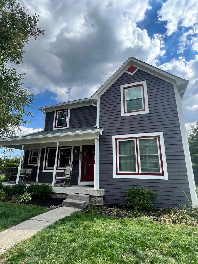 A gray house with red trim and a porch on a cloudy day.