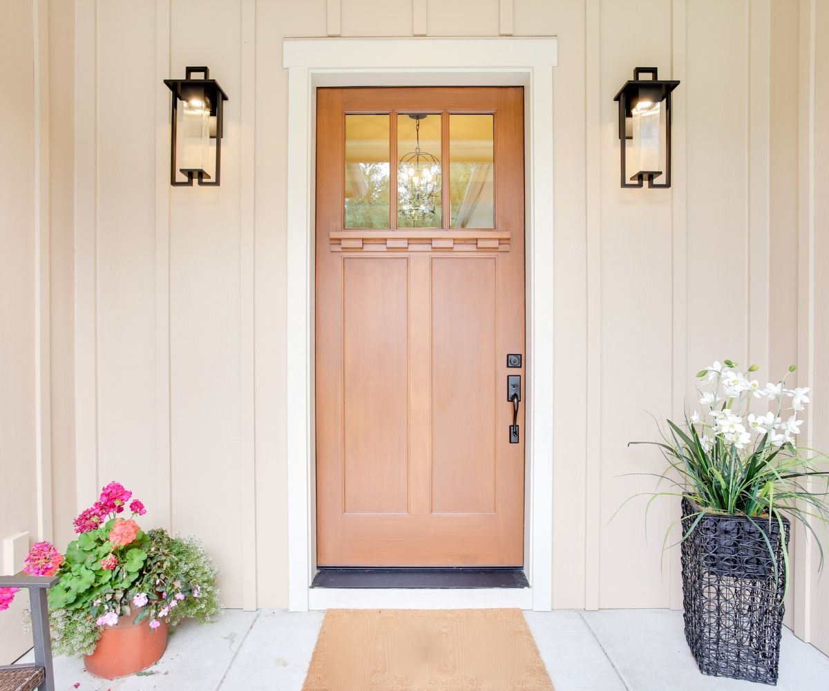 The front door of a house with a wooden door and two lanterns on the wall.