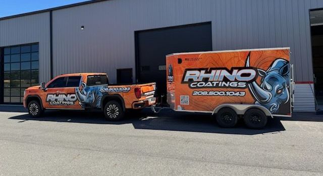 Two rhino coatings trucks are parked in front of a building.