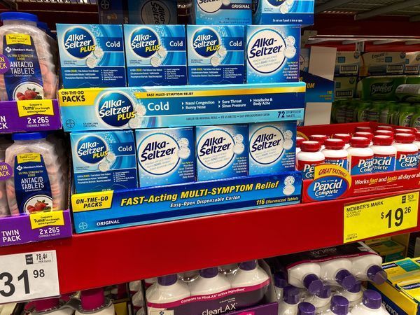 Gloved hand holding a COVID-19 test tube with a microscope in the background. Tube has purple cap and blood sample.