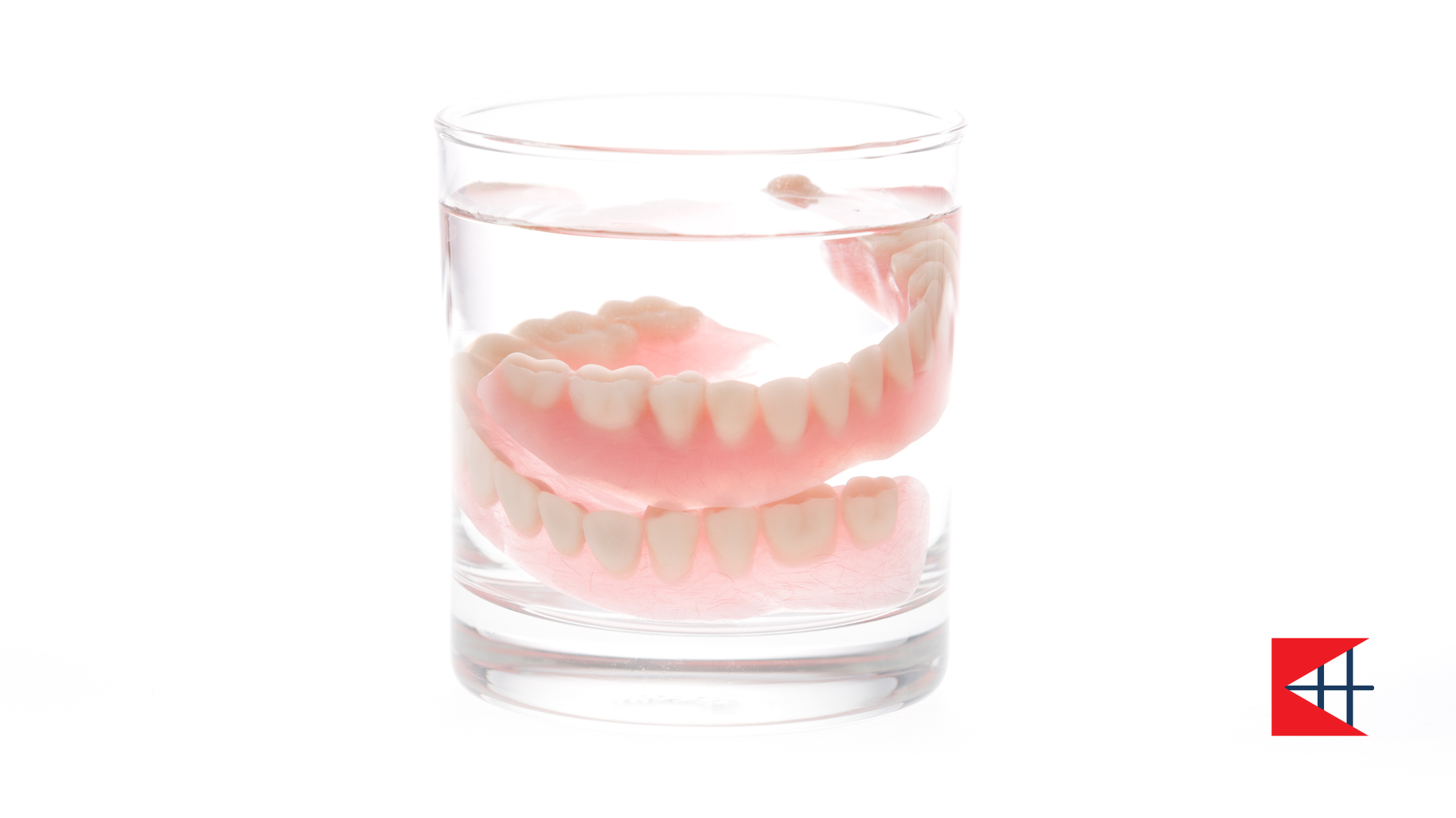 Dentures soaking in a glass of clear liquid. White and pink false teeth.
