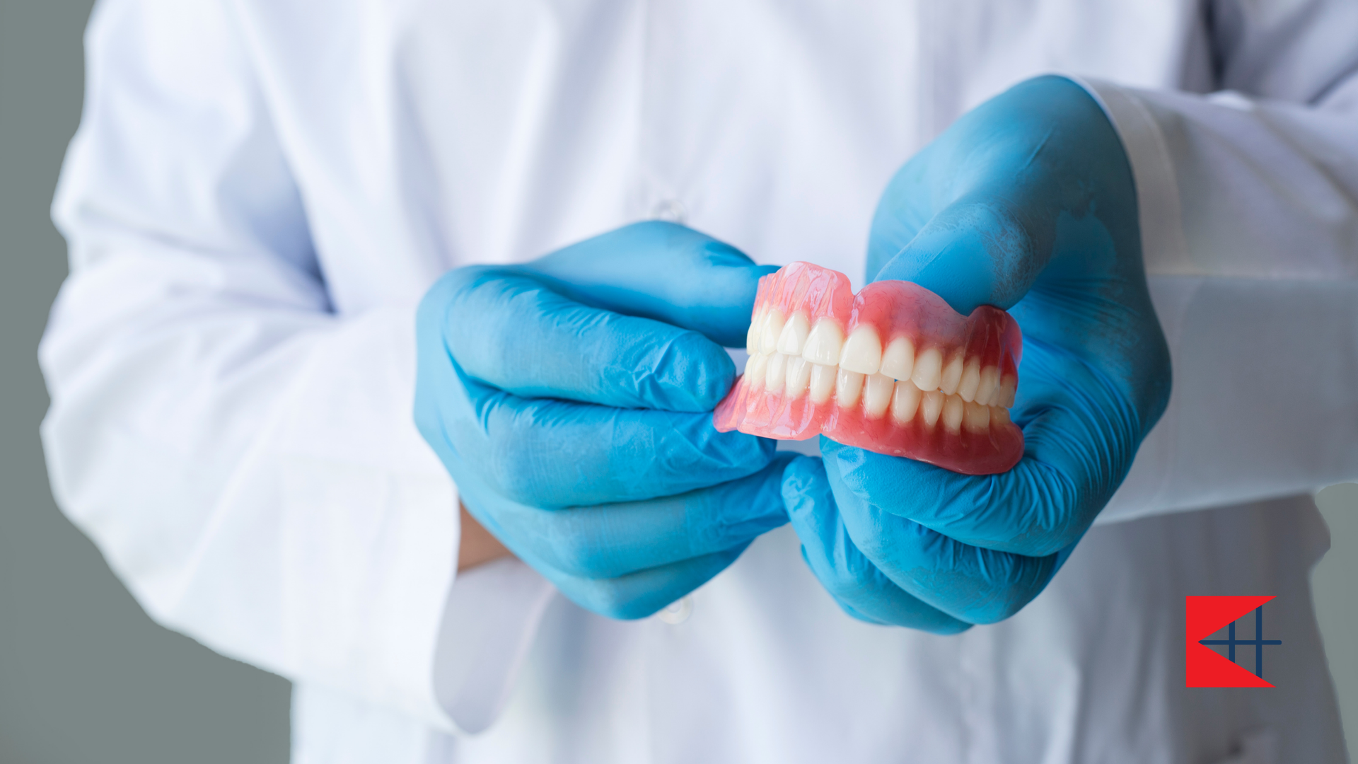 A dentist wearing blue gloves is holding a denture in his hands.