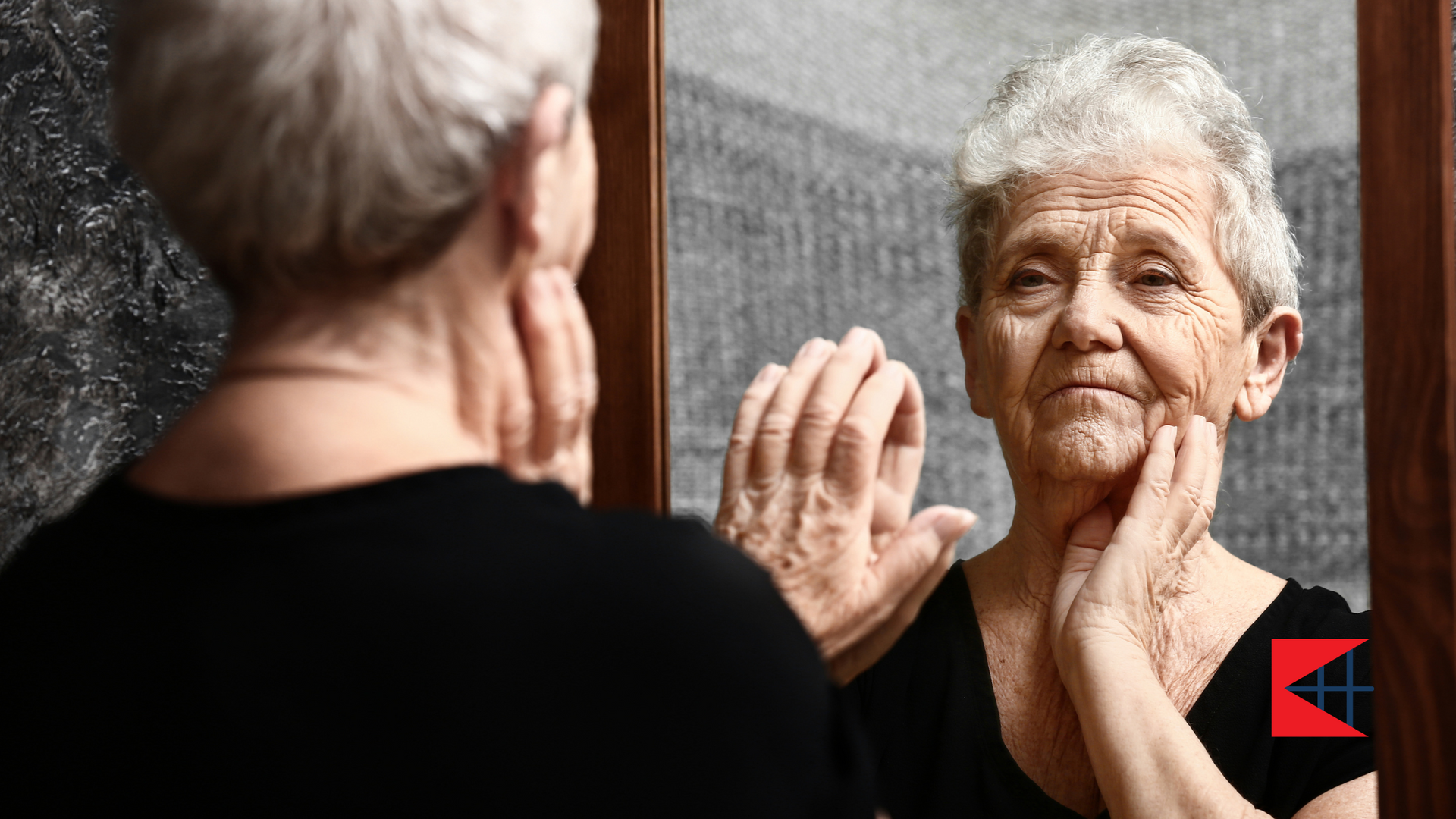 An elderly woman is looking at her reflection in a mirror.