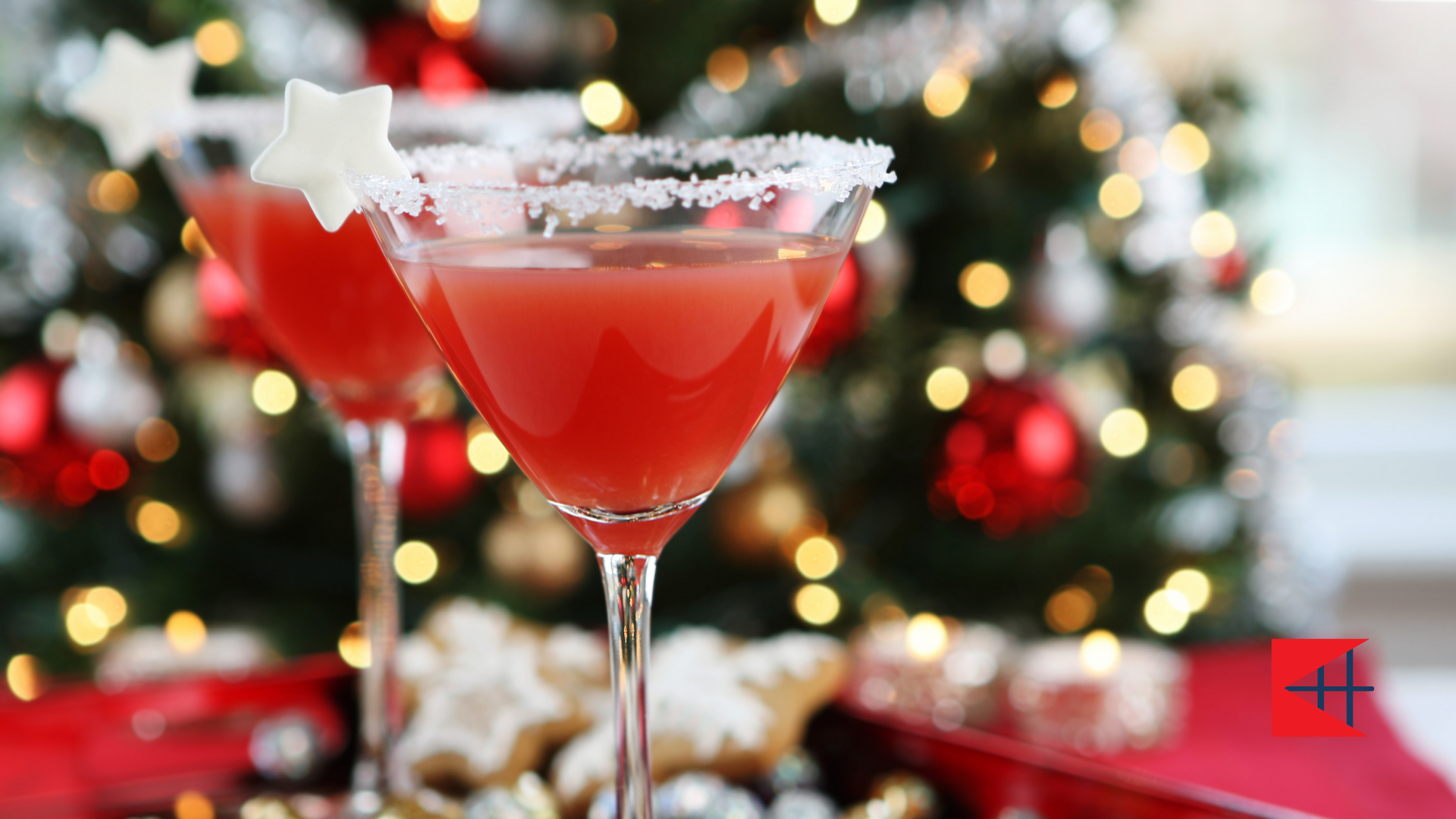 Two martini glasses filled with red liquid in front of a christmas tree.