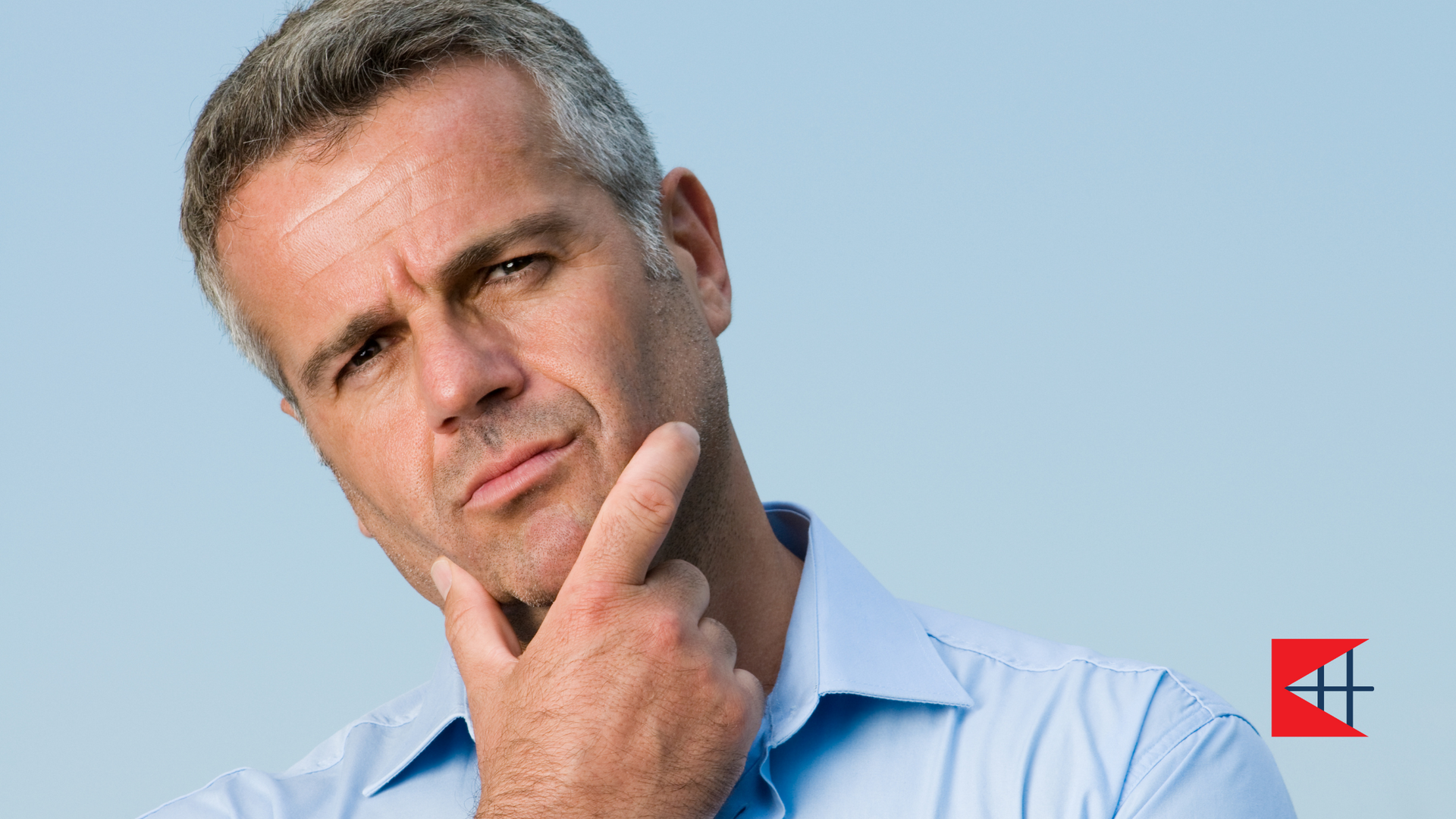 A man in a blue shirt is thinking with his hand on his chin.