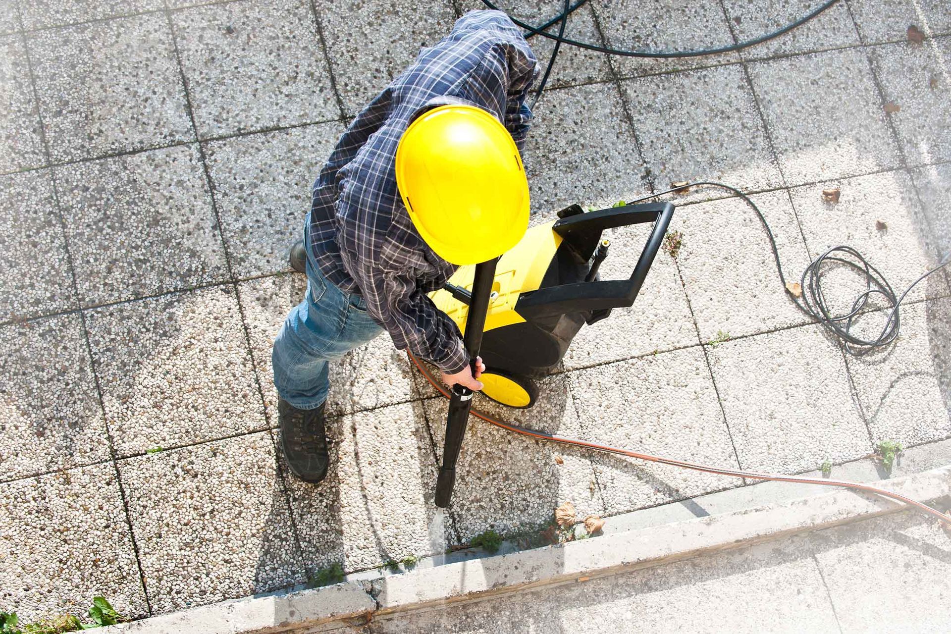 Person in yellow hard hat power washing a paved patio.