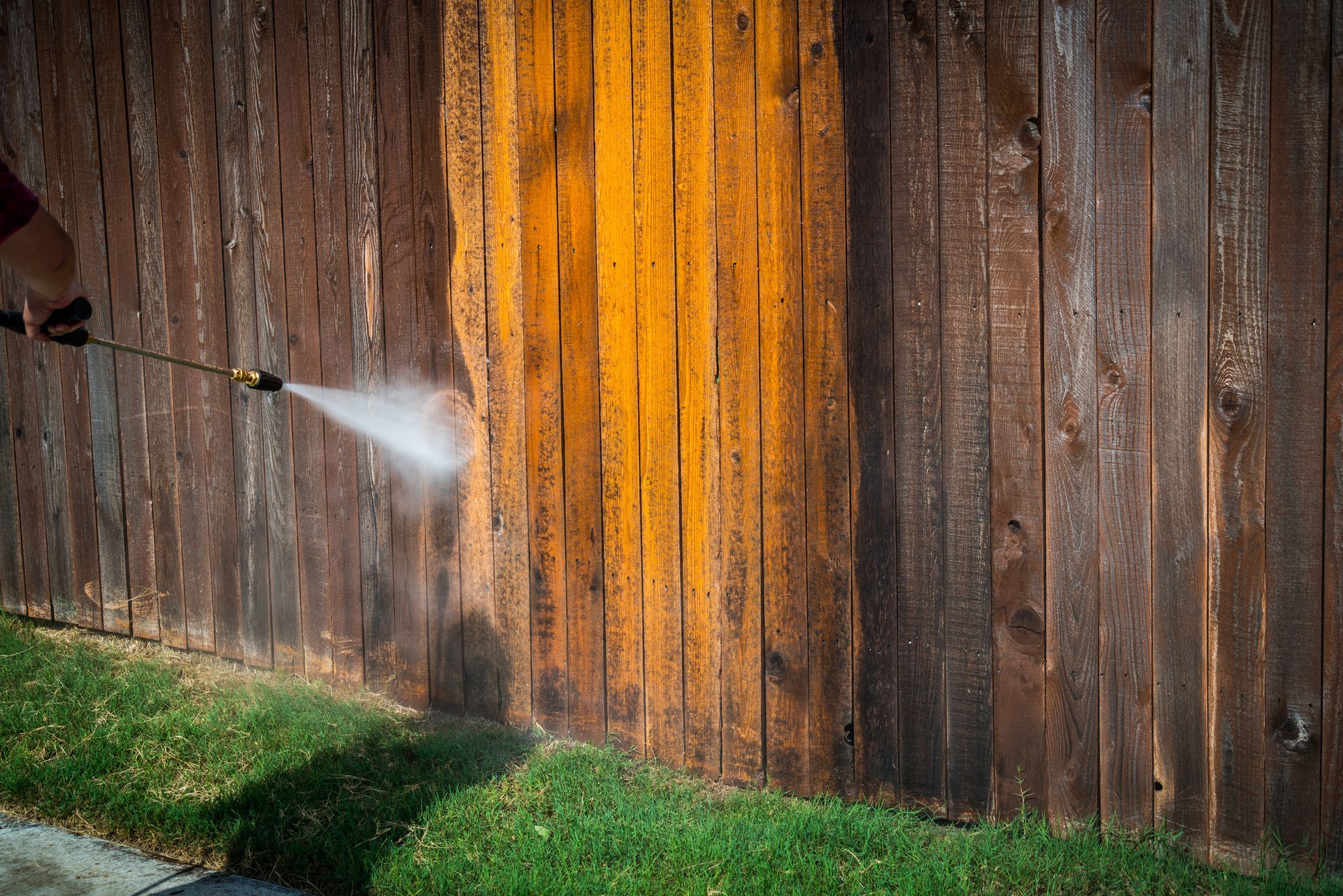 Pressure washing a wooden fence, revealing cleaner wood.