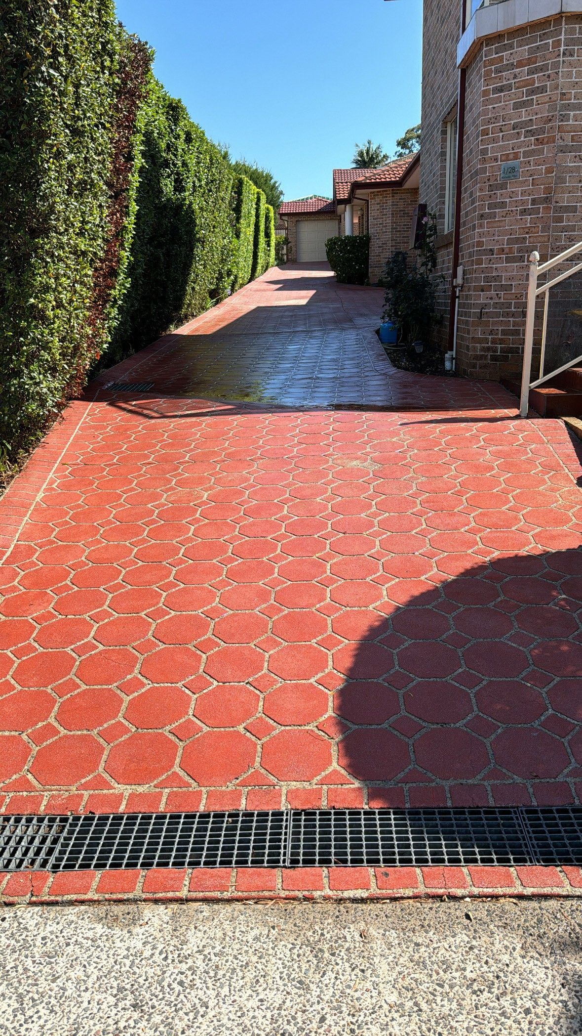 Concrete driveway and sidewalk next to a grassy area. Gates and cars in the background.