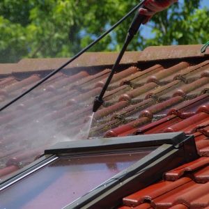Pressure washing a red tiled roof, next to a skylight.