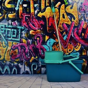 Mop and bucket in front of graffiti-covered wall; turquoise bucket, graffiti in bright colors on a wooden floor.